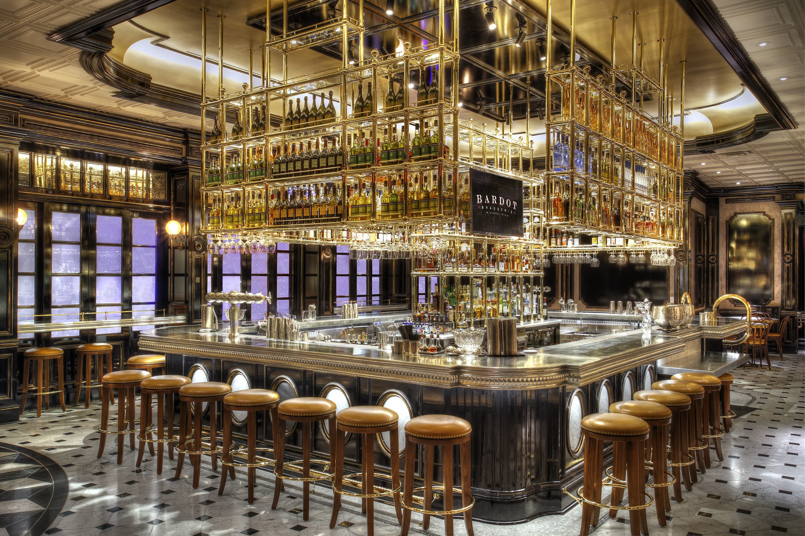 Hotel bar with a metal bar top beneath brass bottle shelving